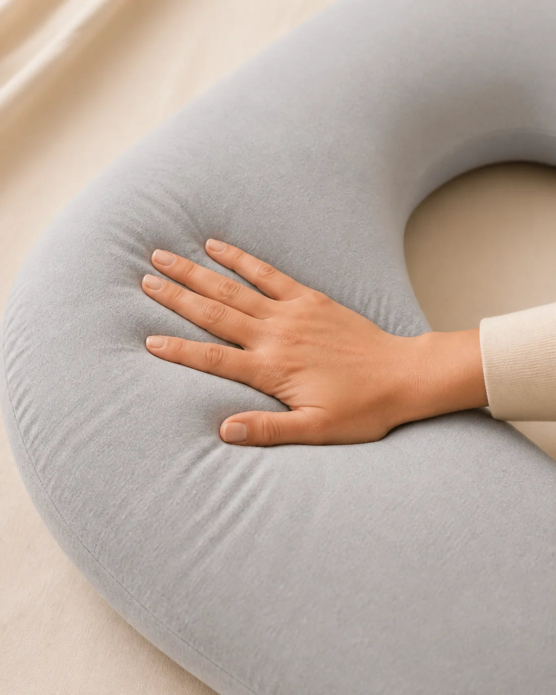 Hand gently pressing into a plush gray pregnancy pillow